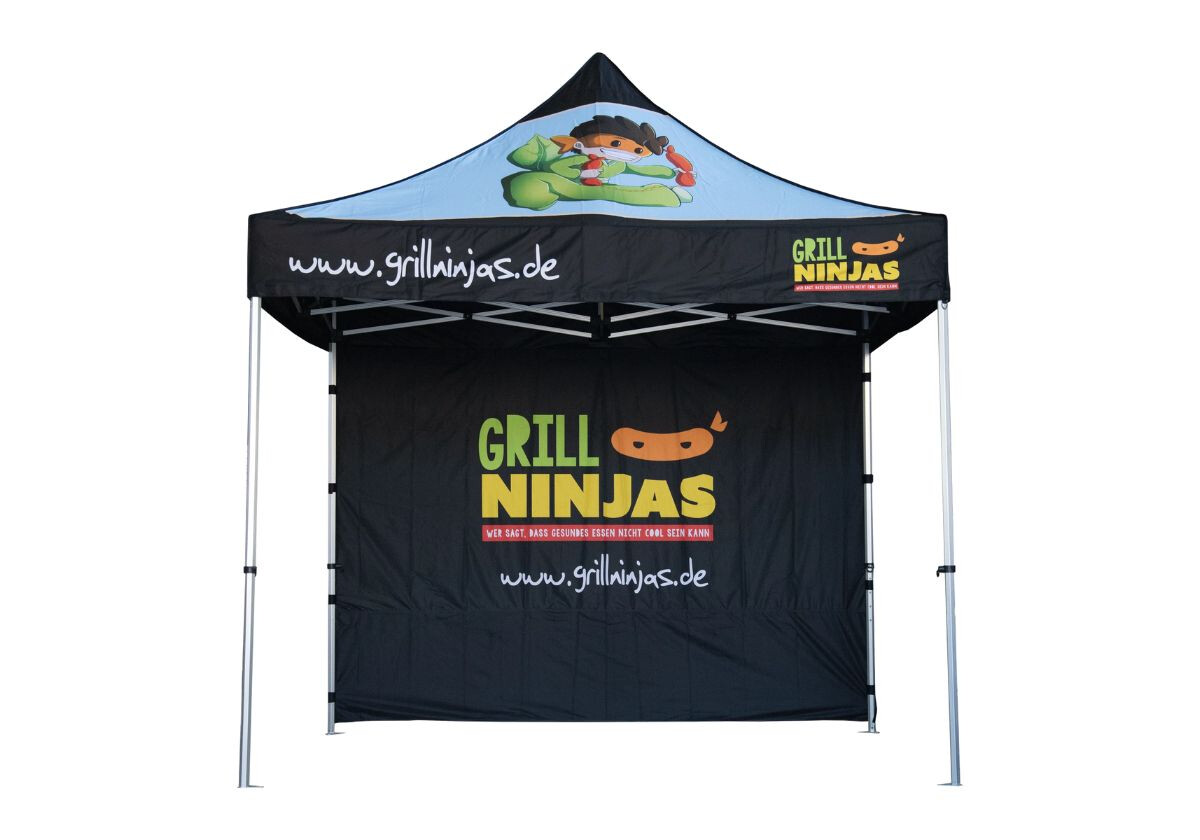 Schwarzes Faltzelt mit der Aufschrift „Grill Ninjas“ und Website-Adresse, darüber ein Comic-Maskottchen in Ninja-Verkleidung mit Gemüse und Grillzange.