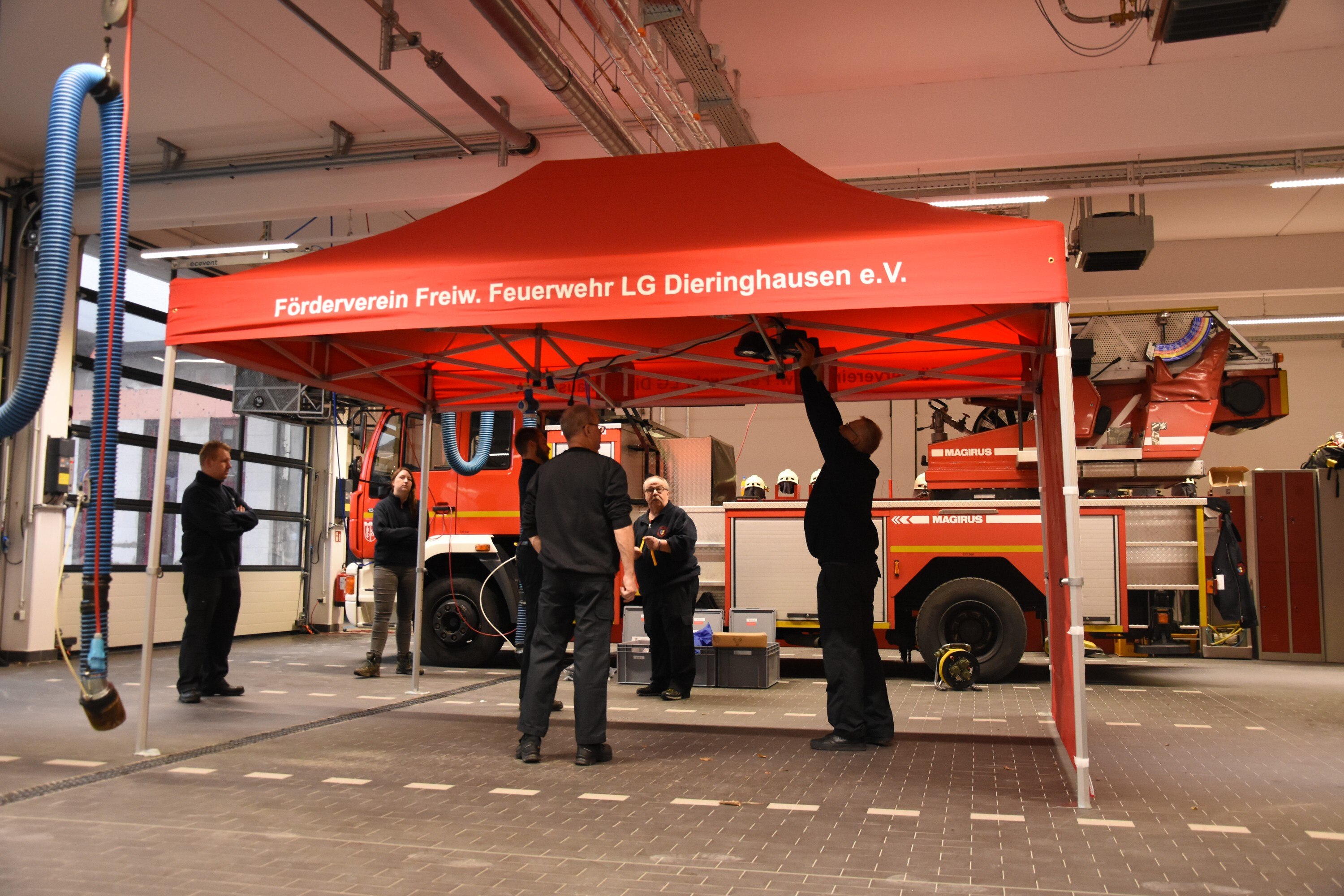 Mehrere Personen beim Aufbau eines roten Duratent Faltpavillons in der Fahrzeughalle